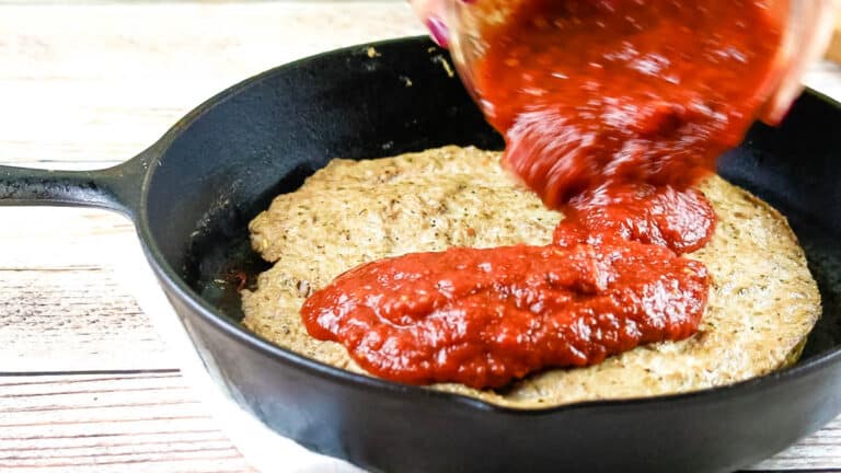 pouring pizza sauce over meat crust