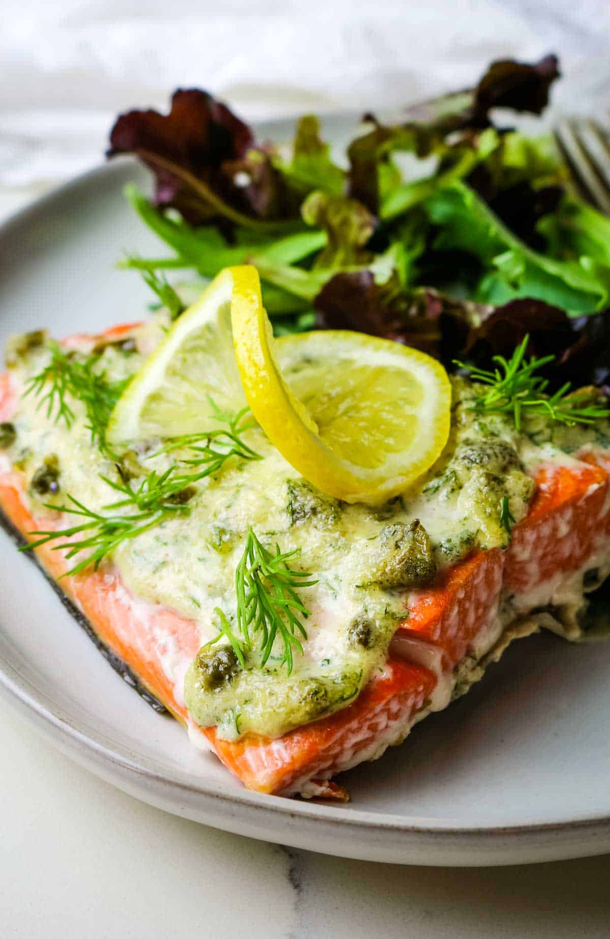 Baked salmon over white plate with lemon slice on top.