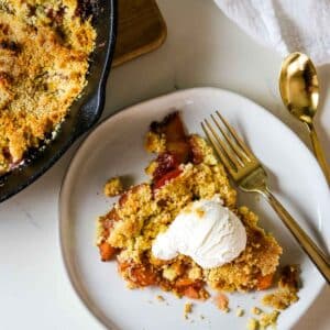 peach cobbler with vanilla ice cream on white plate.