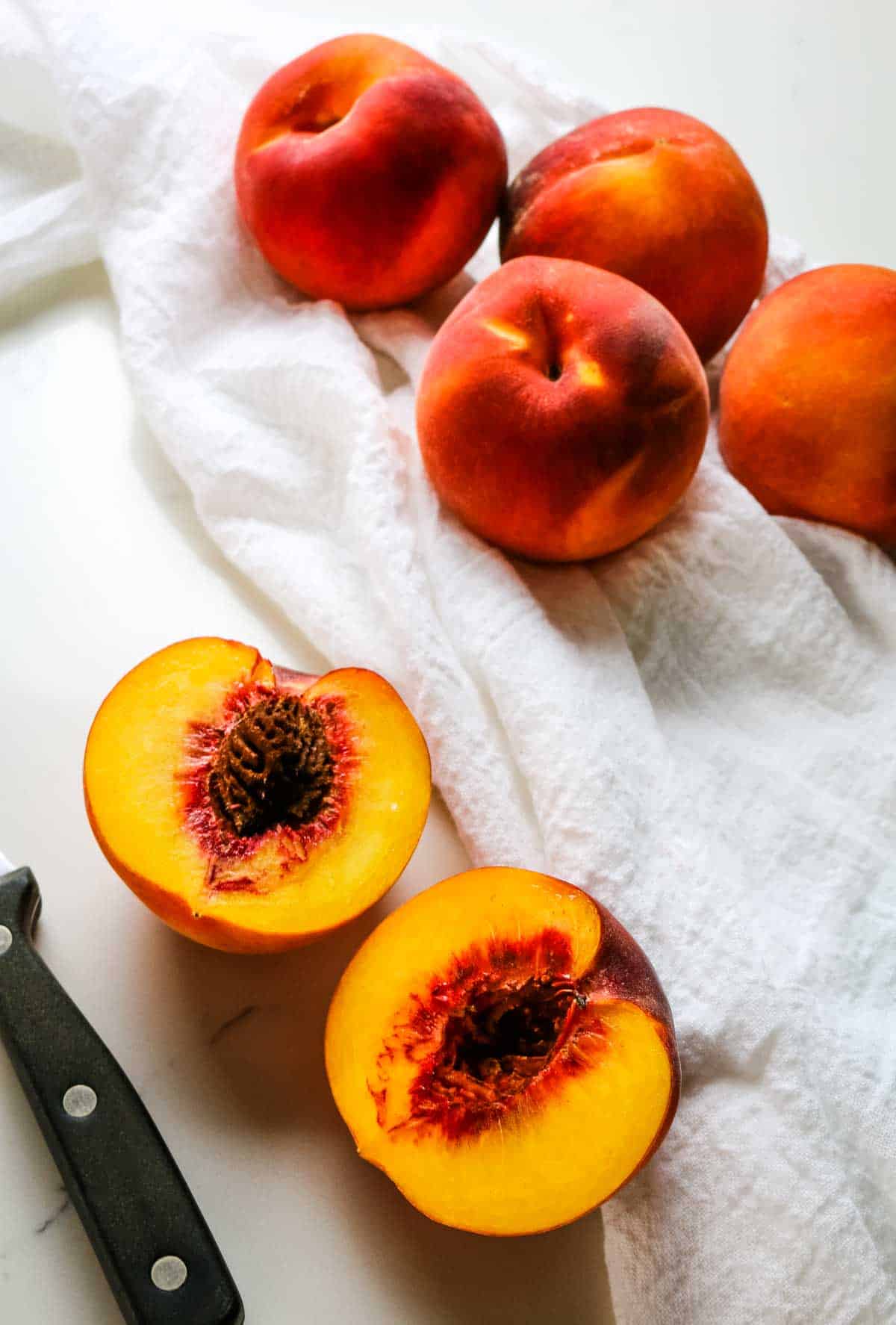 yellow peaches on white towel with paring knife on side