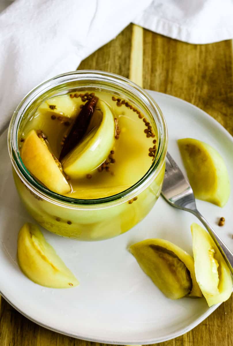 fermented green tomatoes in weck jar on white plate.