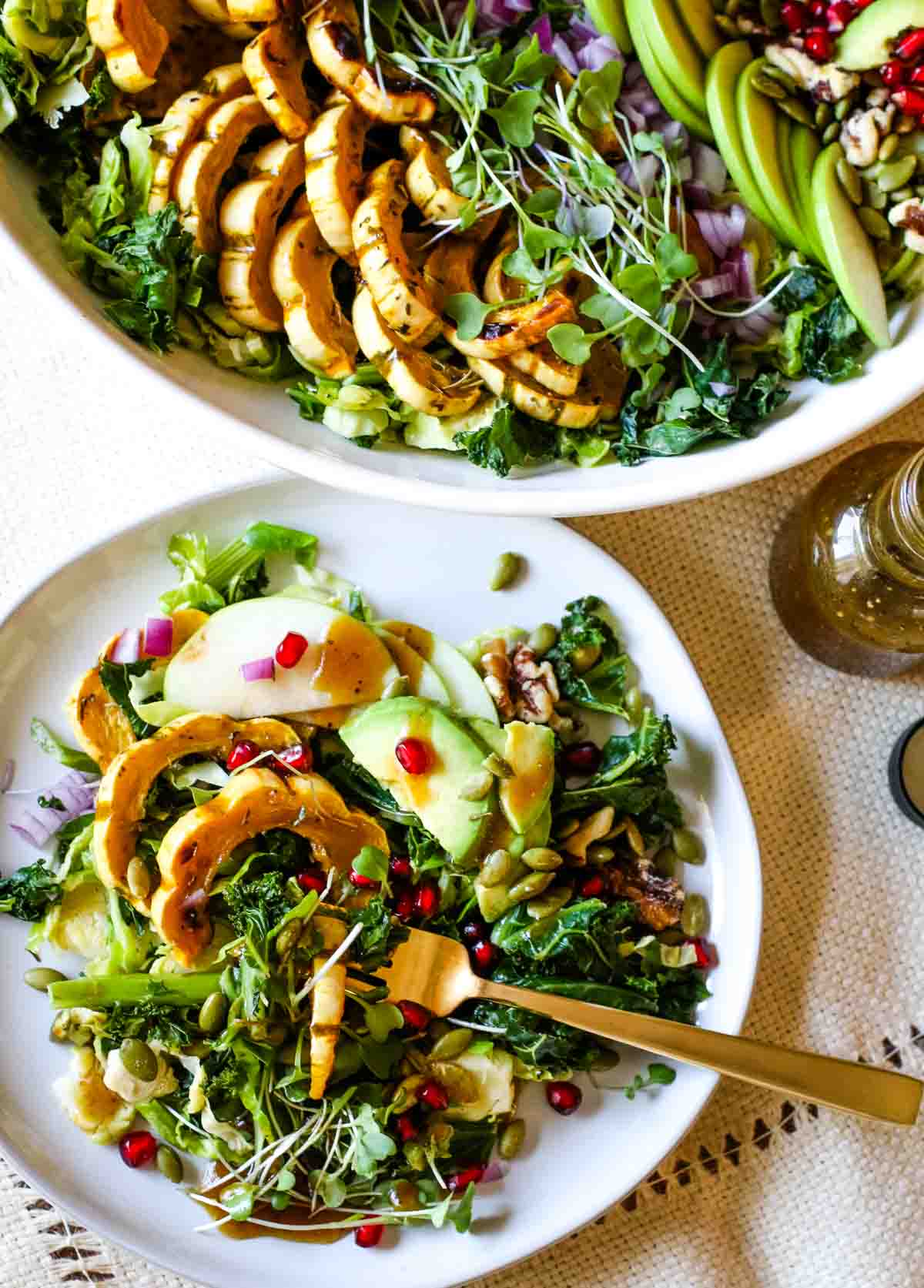 kale salad with delicata squash on a white plate with bowl of salad to the side.