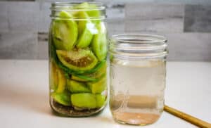 green tomatoes with salt brine in a jar and wooden spoon.