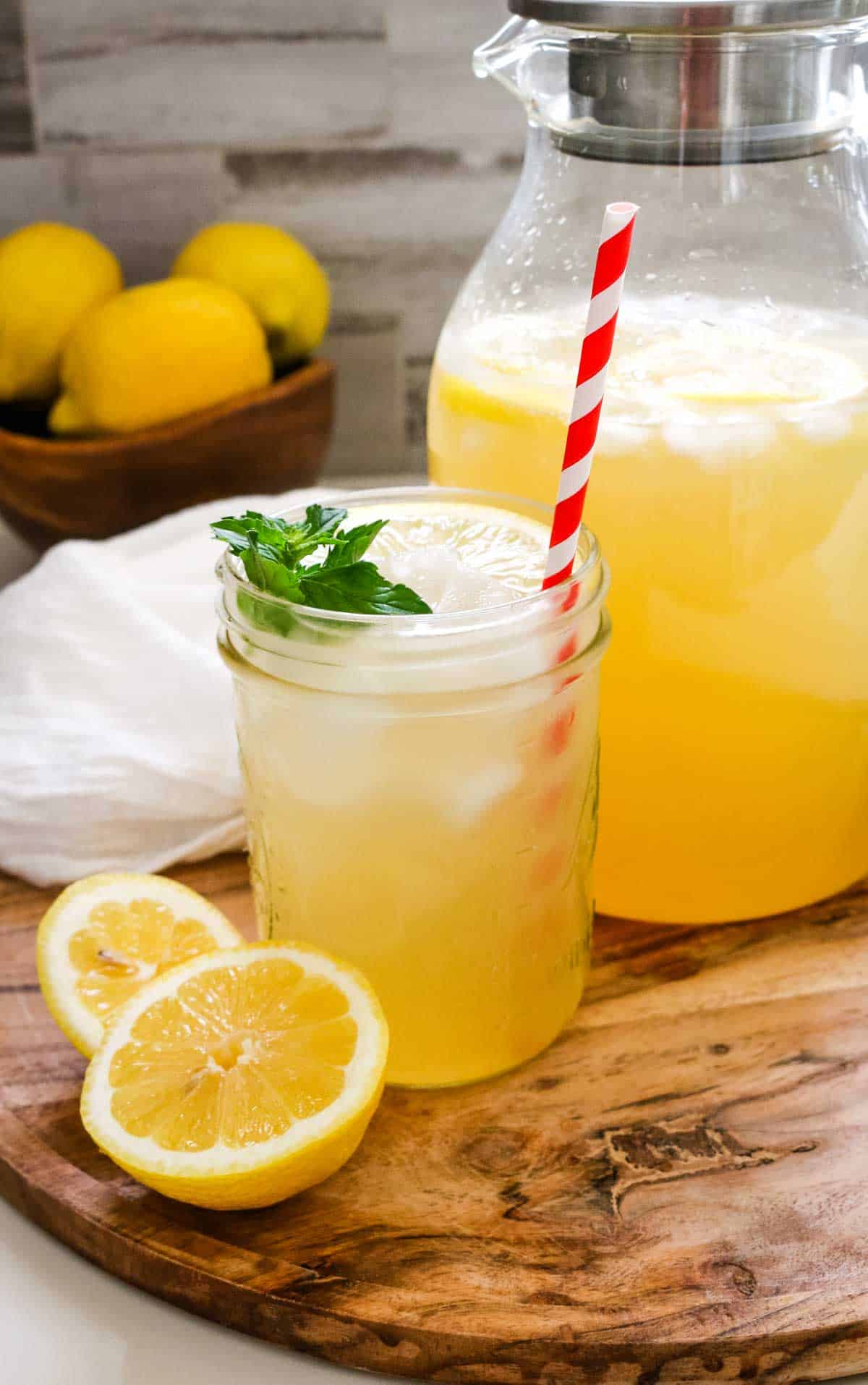 fresh lemons cut in half and pitcher of lemonade in background on wooden board.