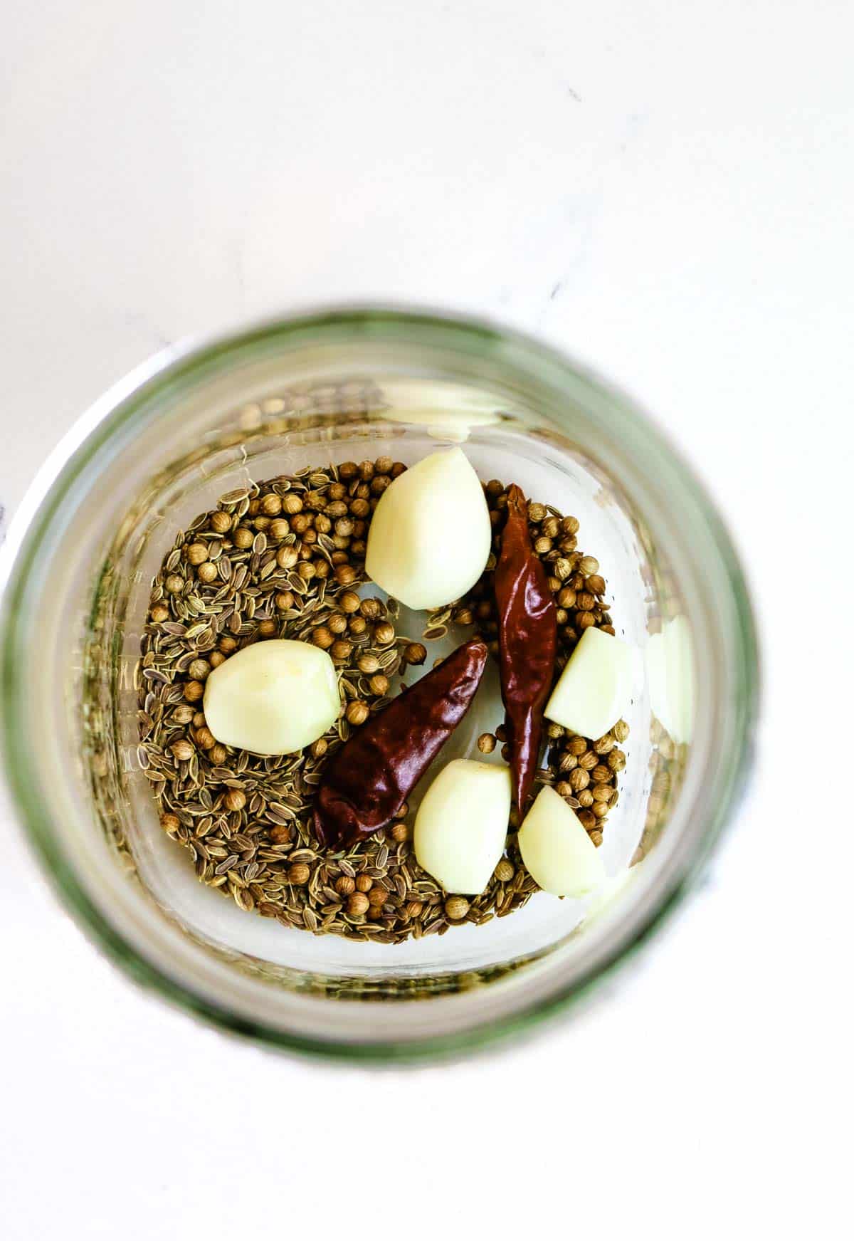 coriander and dill seeds in a mason jar with garlic and peppers.