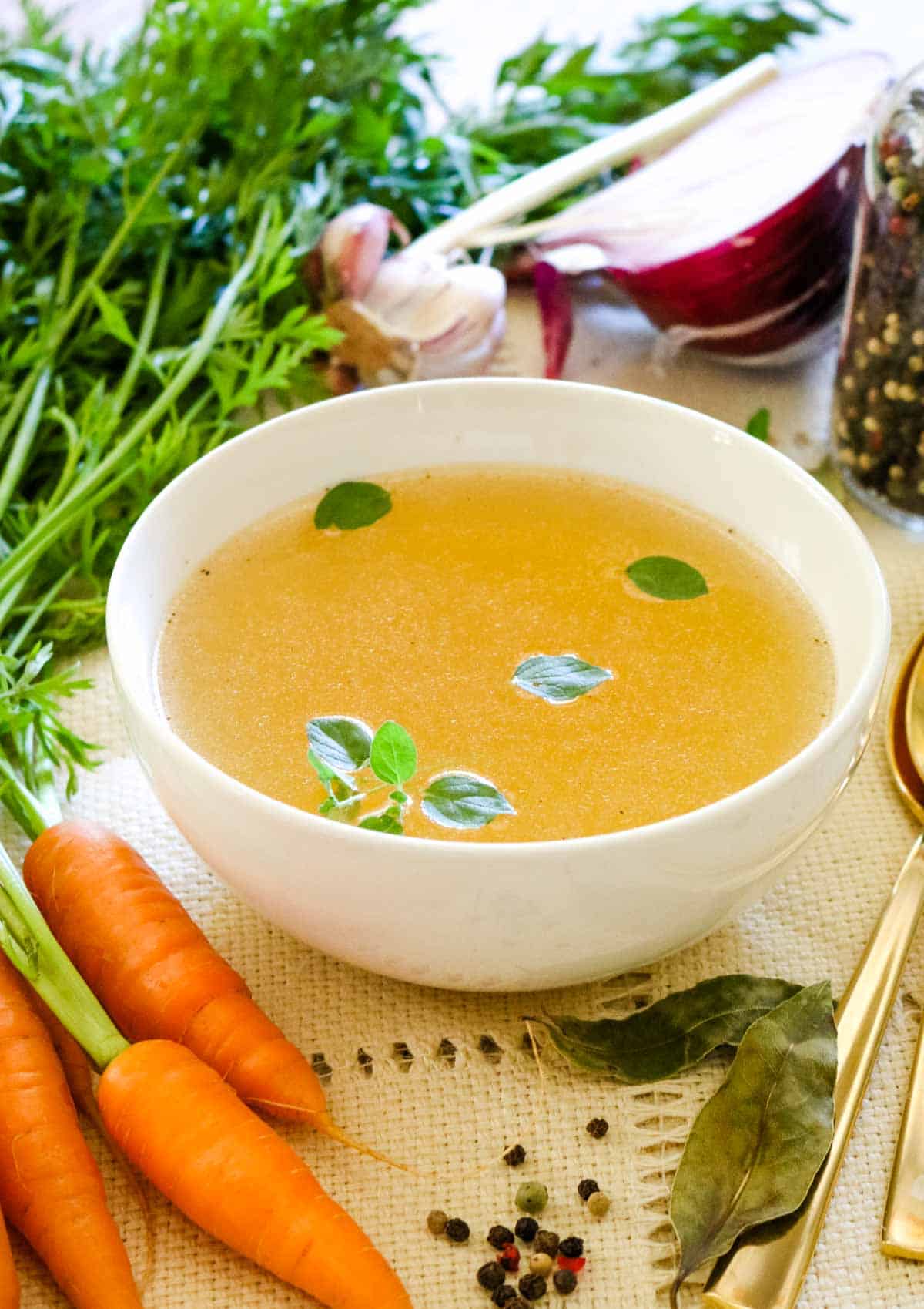 broth in white bowl with onions carrots and bay leaves.