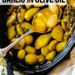 garlic in oil in black dish with text overlay: "How to Roast Garlic in Olive Oil"