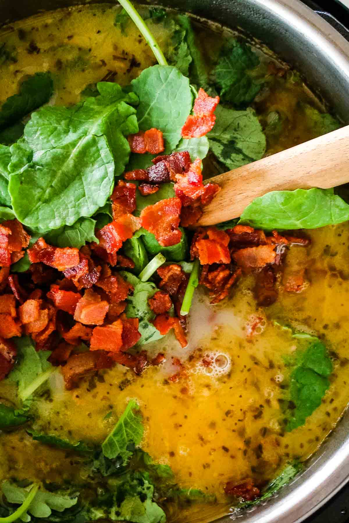 adding baby kale and bacon bits to zuppa toscana and stirring with wooden spoon.