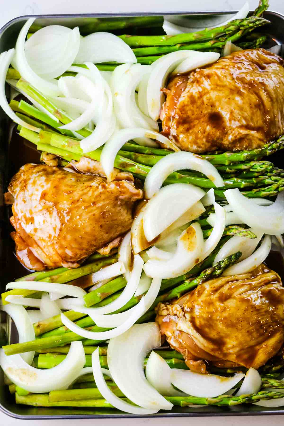 chicken thighs tucked in between asparagus and onions.