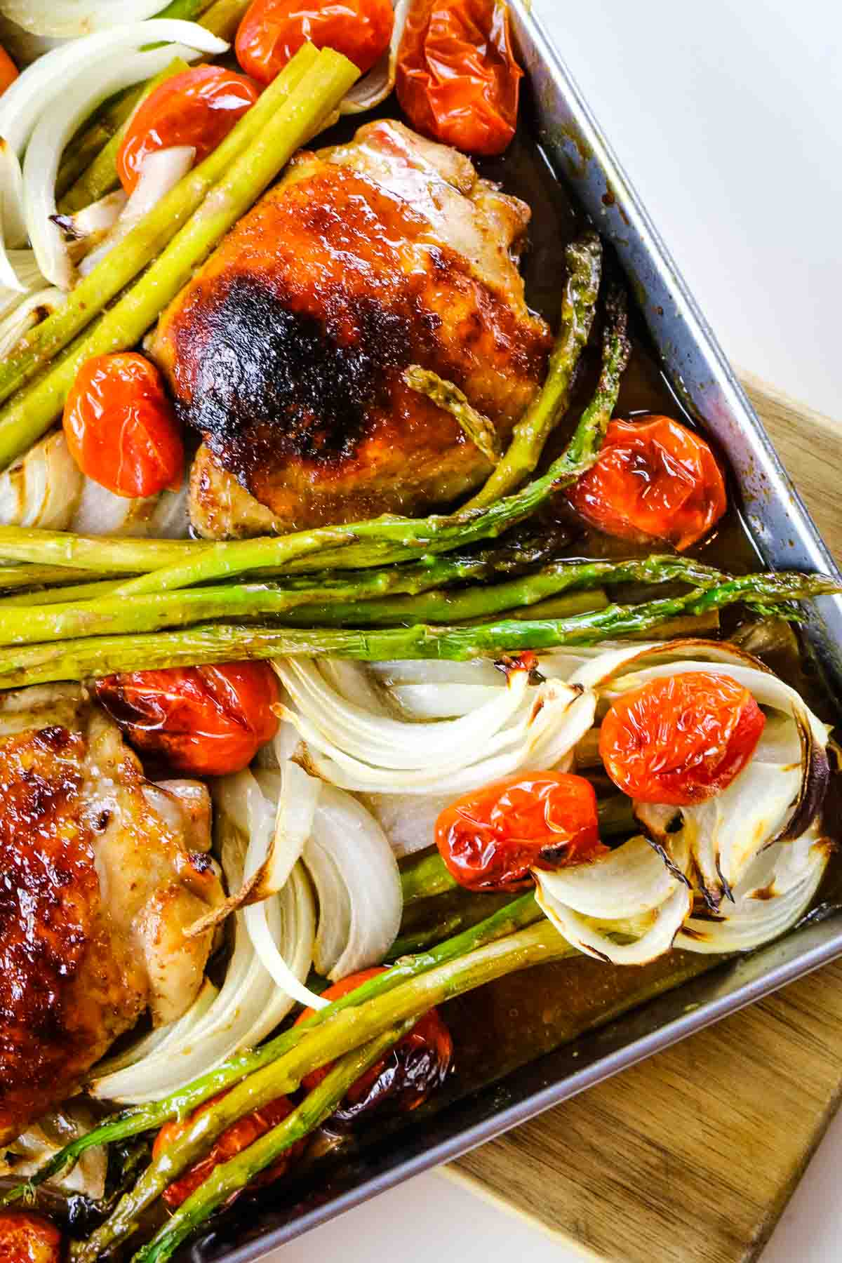 chicken with asparagus, tomatoes, and onions on sheet pan.