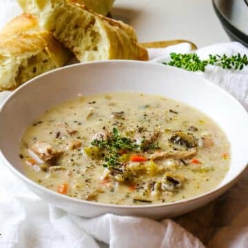 Creamy chicken wild rice soup in white bowl with crusty bread.