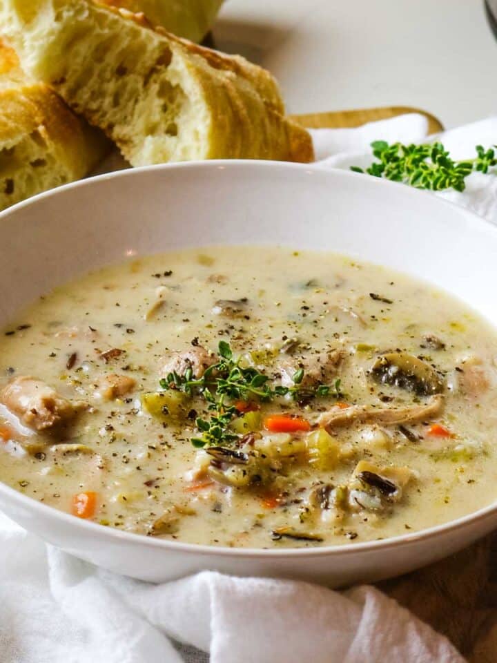 Creamy chicken wild rice soup in white bowl with crusty bread.