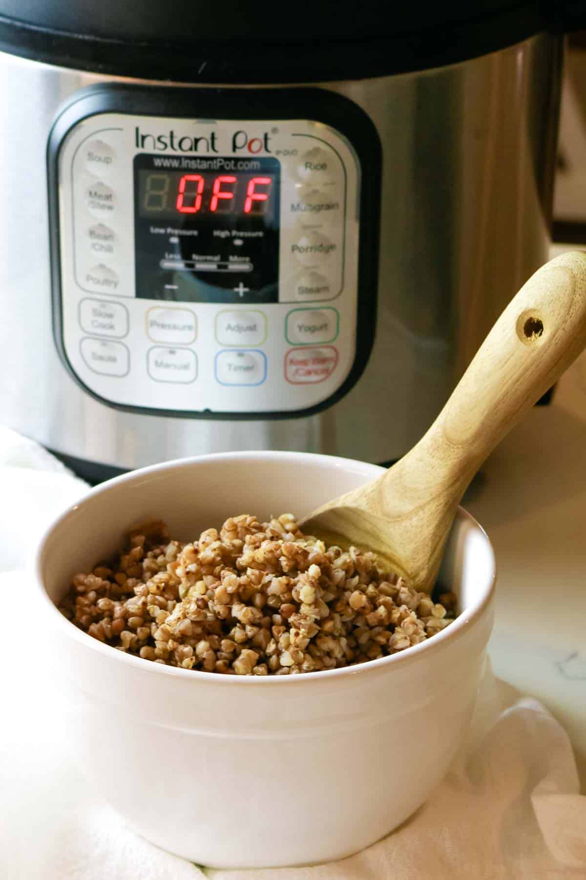 Buckwheat in white bowl with wooden spoon and Instant Pot in background