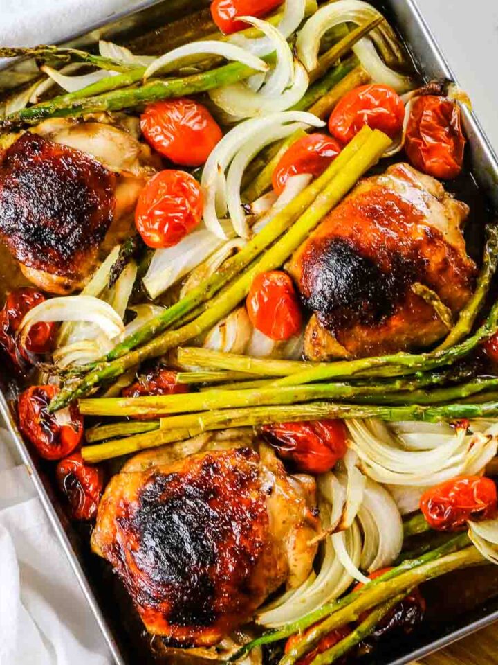 golden brown balsamic chicken roasted on sheet pan with asparagus, tomatoes, and onions.