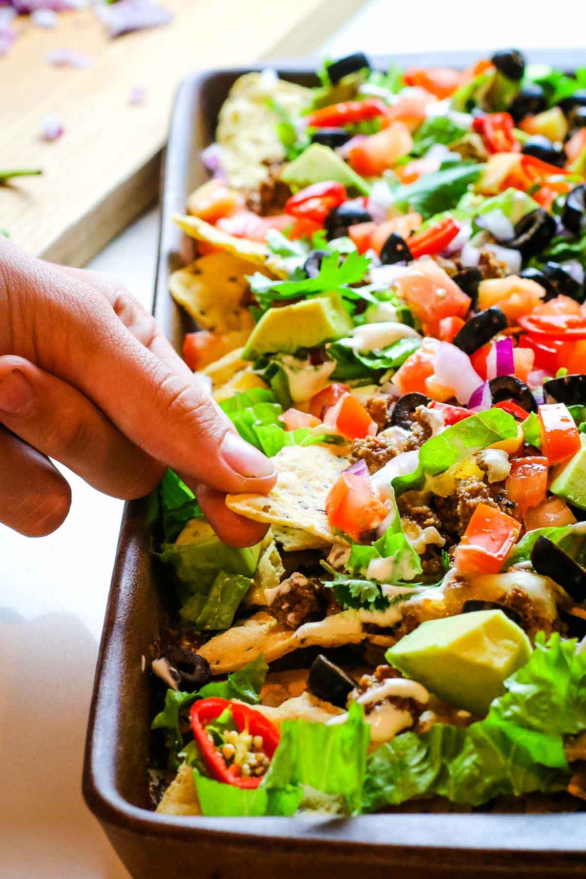 sheet pan nachos with hand pulling a chip.