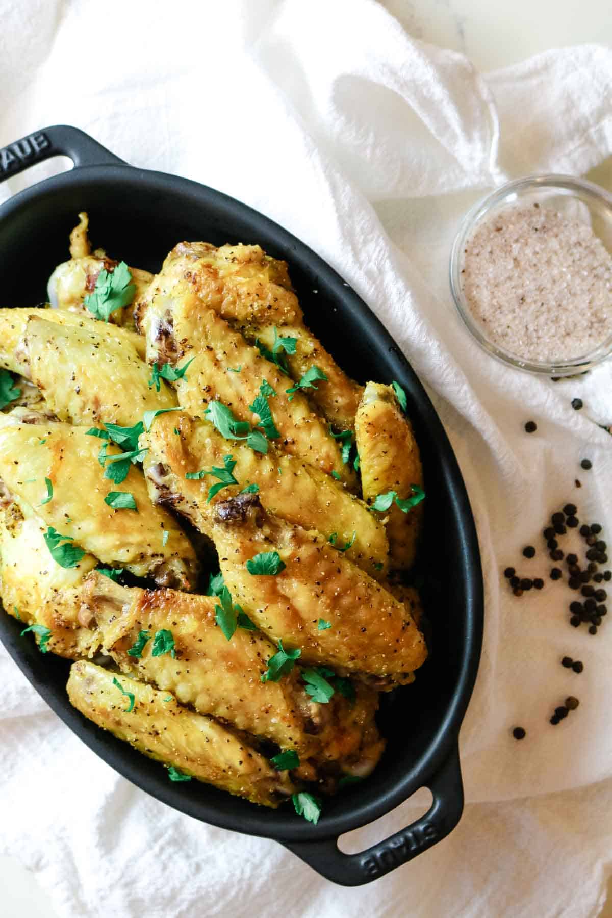 Chicken wings in a black dish with peppercorns and salt to the side.