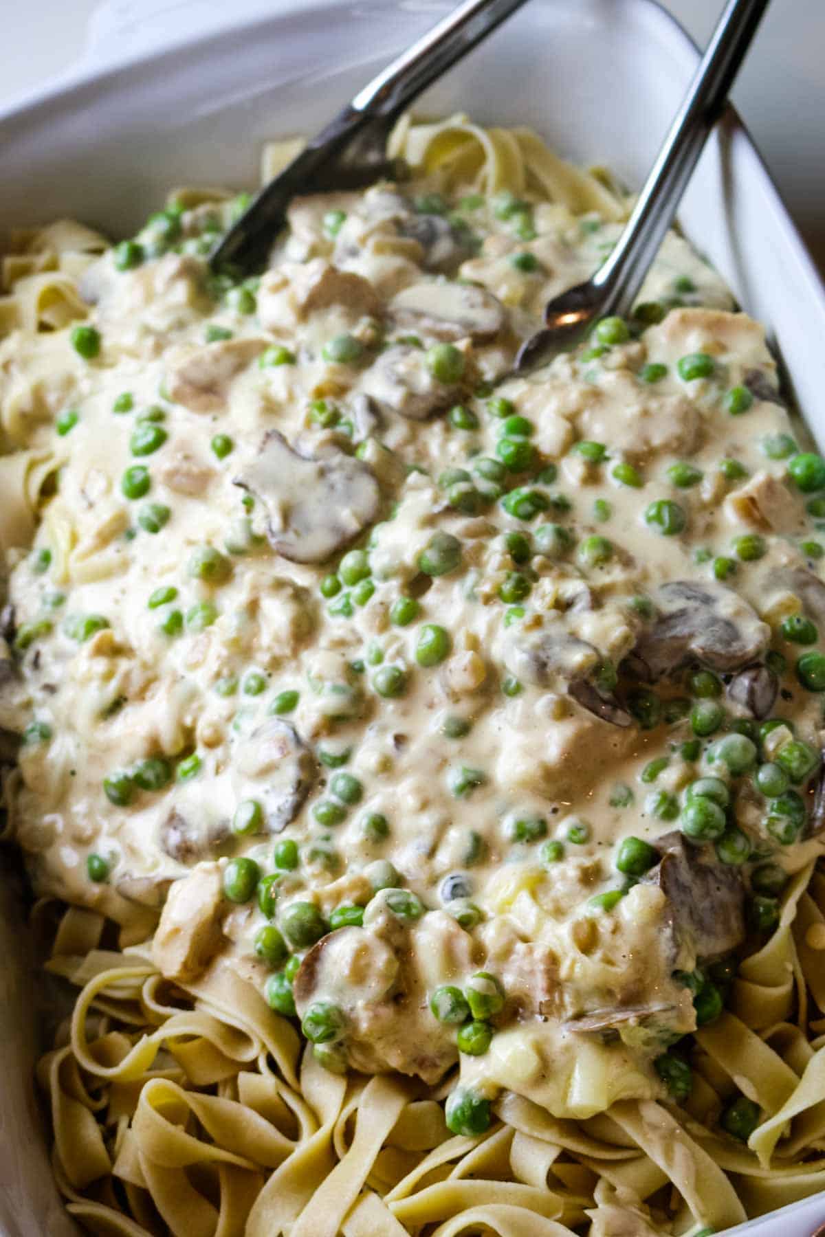 noodles and tuna casserole sauce in white dish with pair of tongs.