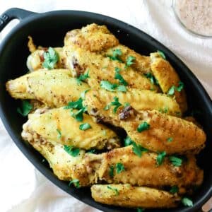 chicken wings on black dish with green herb.