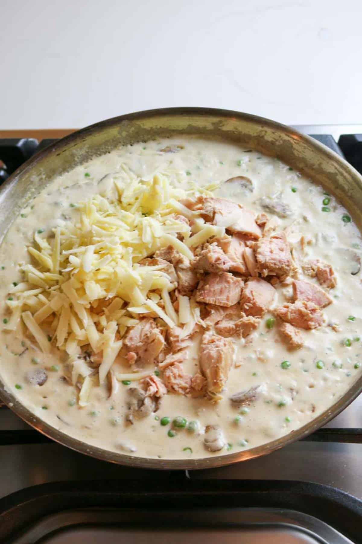 flaky tuna with cheese added to creamy mixture in skillet.