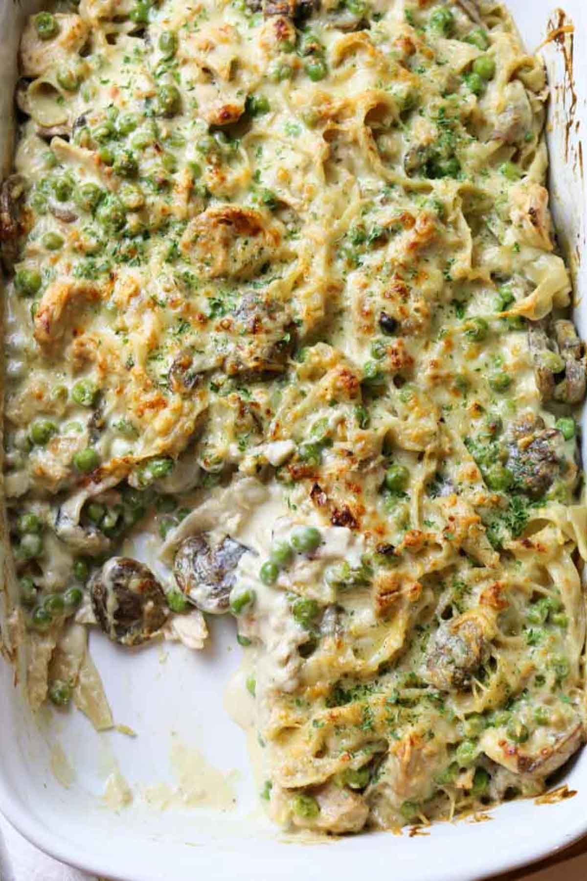 tuna noodle casserole with mushrooms and peas in white dish.