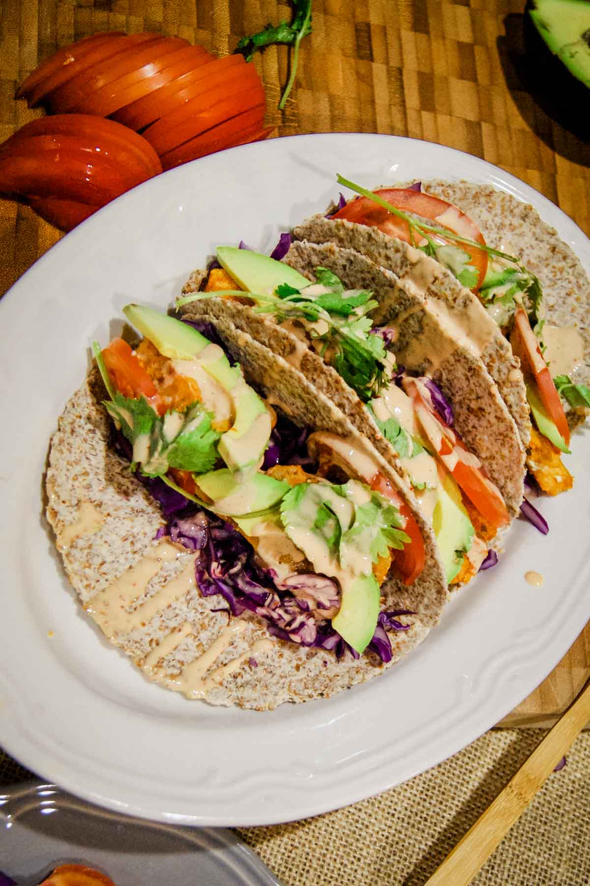 cod fish tacos in sprouted flour tortilla on white platter with tomato on the side.