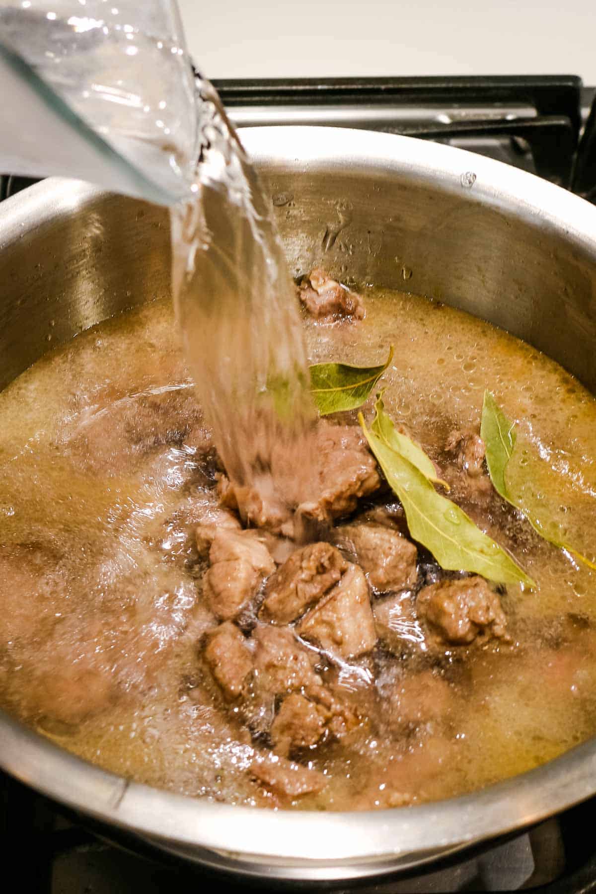 adding water to browned lamb in Uzbek lamb soup.