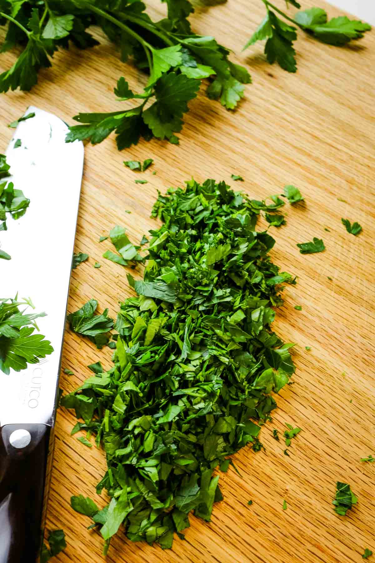 Chopped fresh parsley on cutting board with knife.