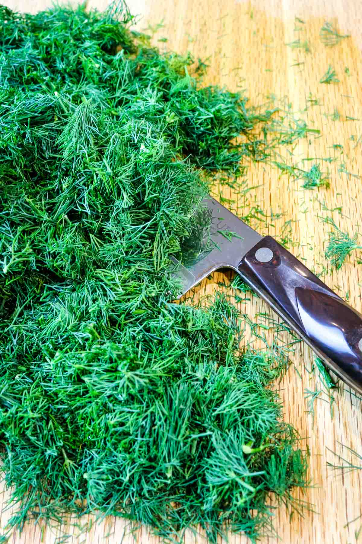 chopped fresh dill on a wooden board with knife to the side.
