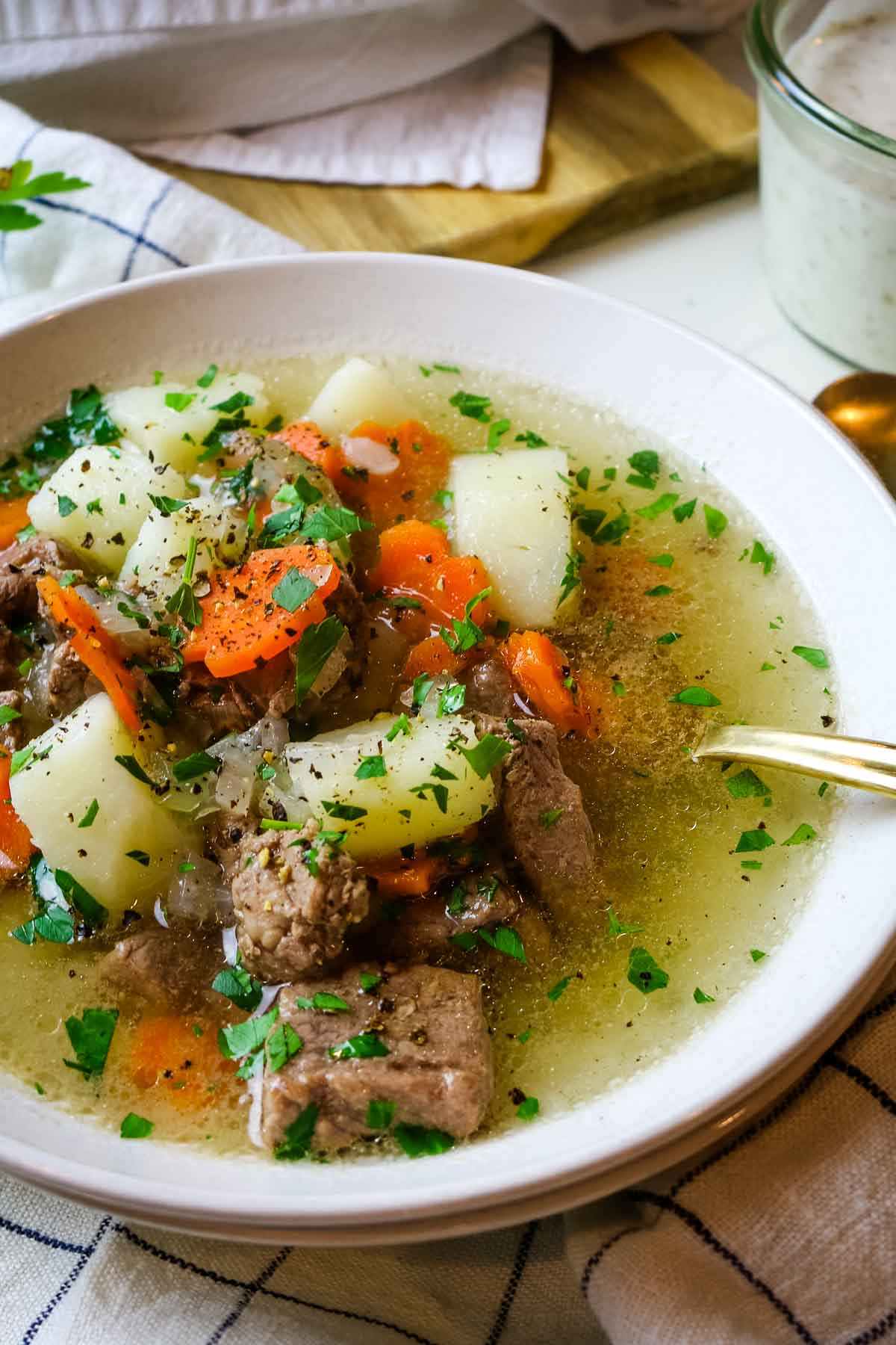 Shurpa soup upclose with lamb, potatoes, and carrots in white bowl.