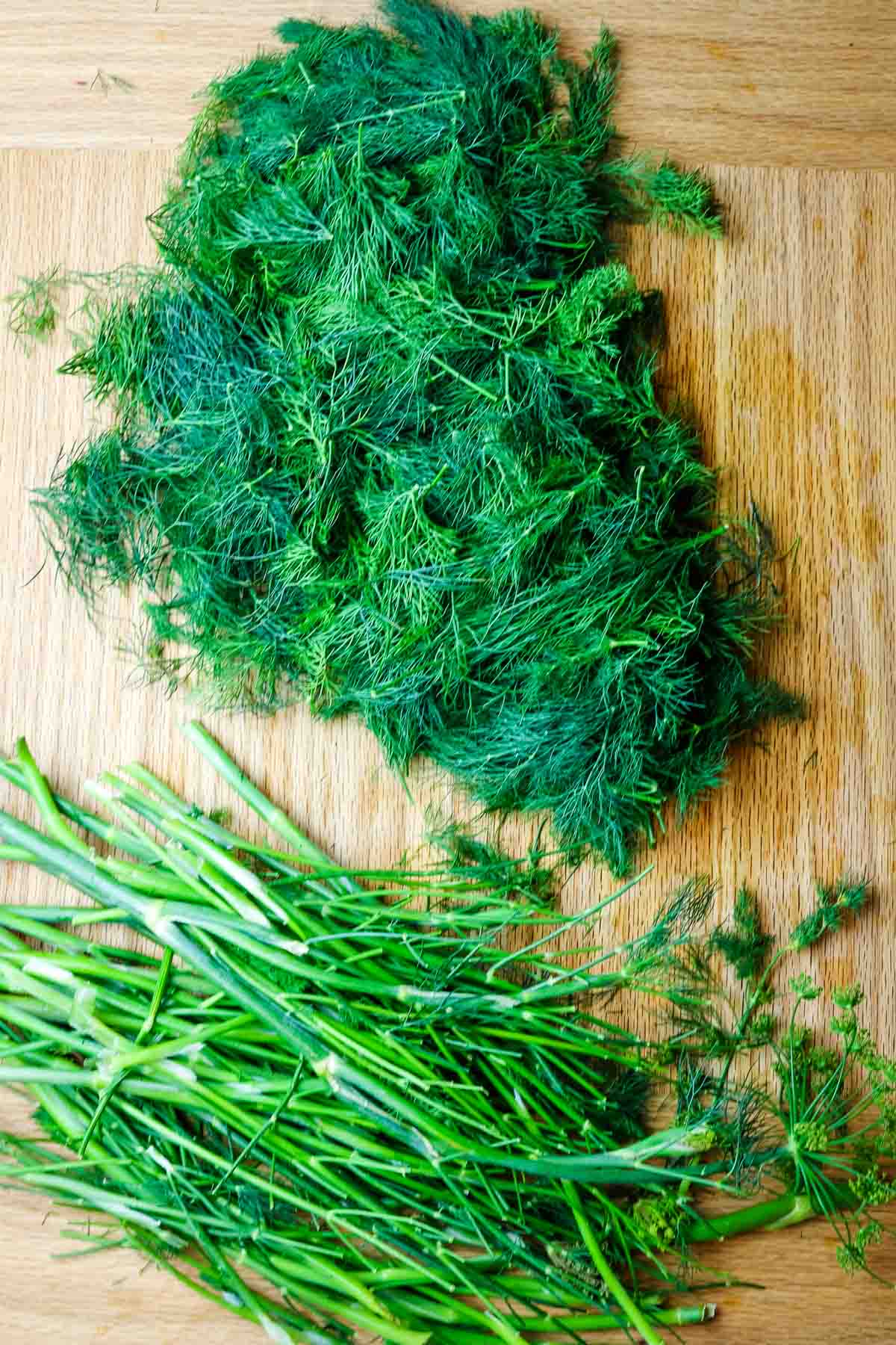 dill weed separated from dill stems on a wooden cutting board.