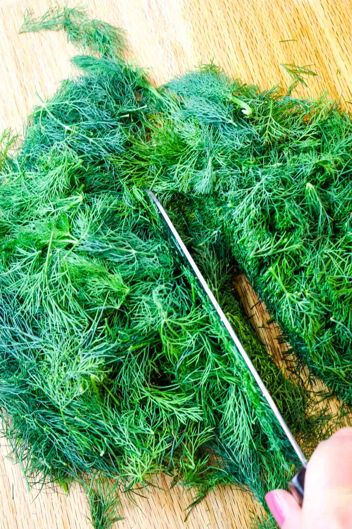 Feathery fresh dill weed chopped on a cutting board with knife to the side. 