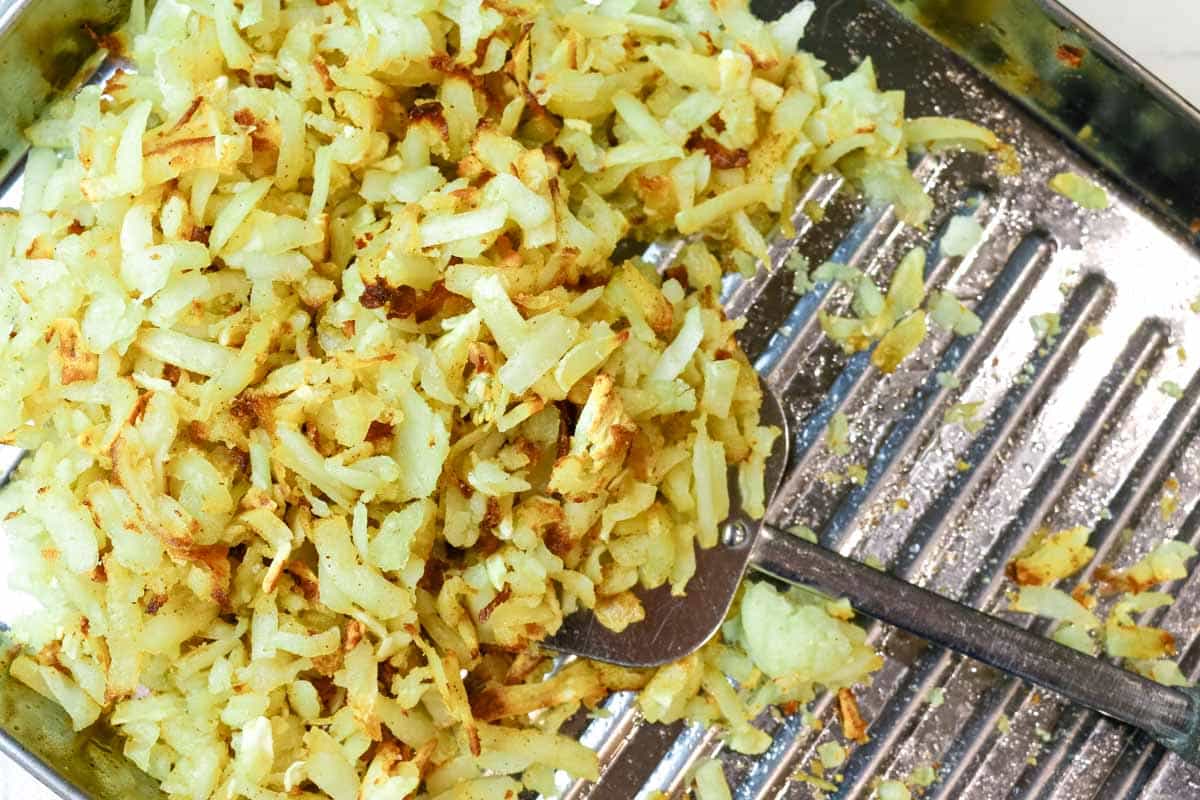 hash browns in cooking sheet with spatula in Perfectly Crispy Shredded Hash Browns in Air Fryer.