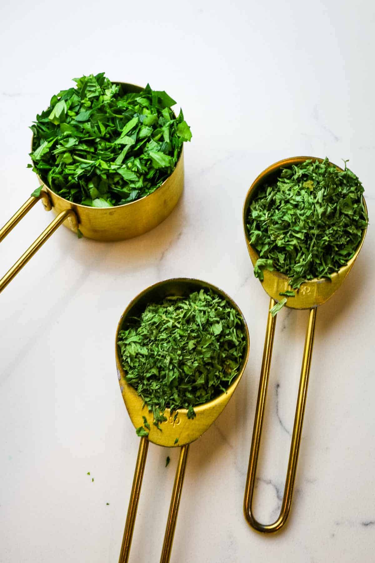fresh parsley and dried parsley in measuring cups and measuring spoons.