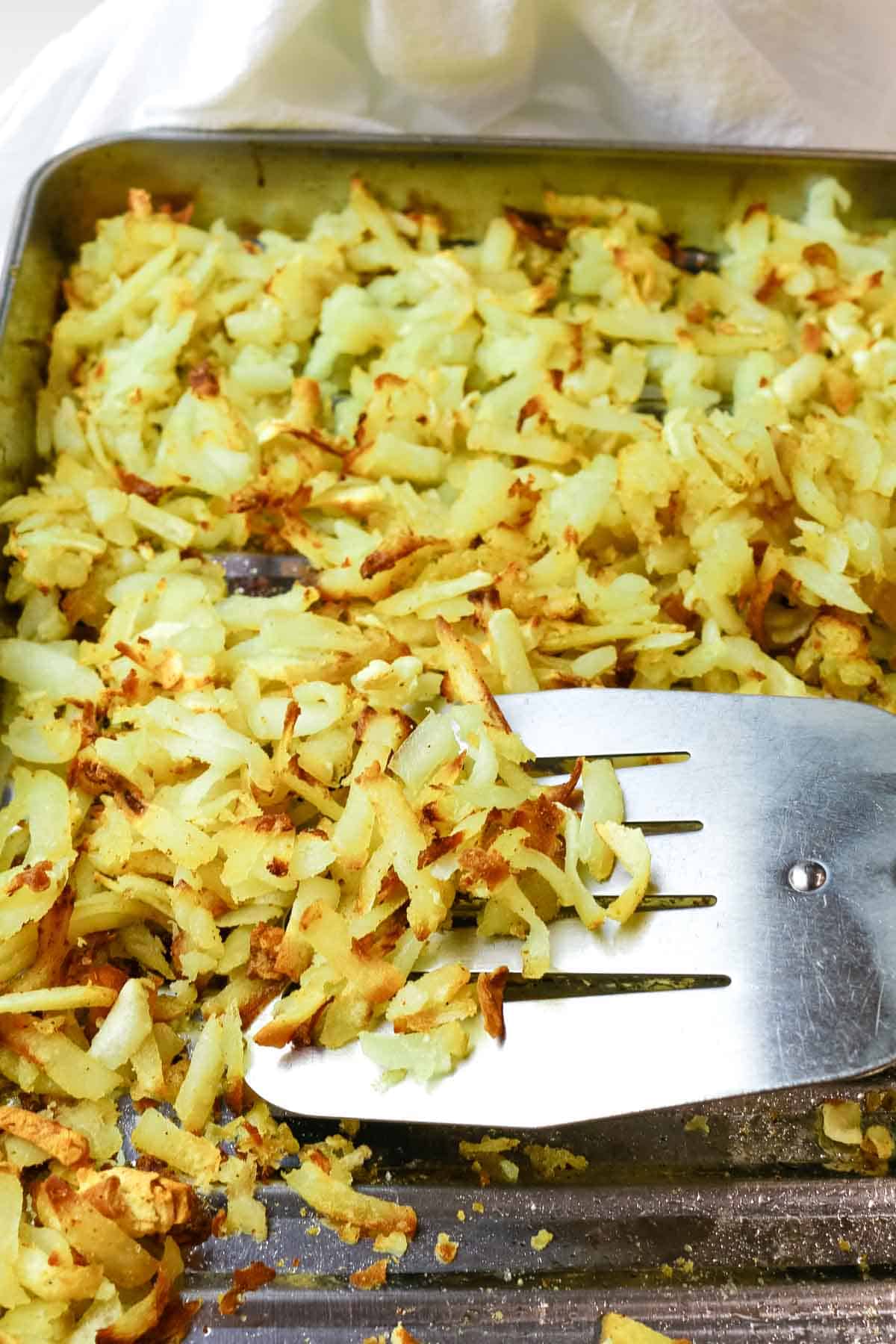 Hash browns on sheet with spatula in perfectly crispy shredded hash browns in air fyer.