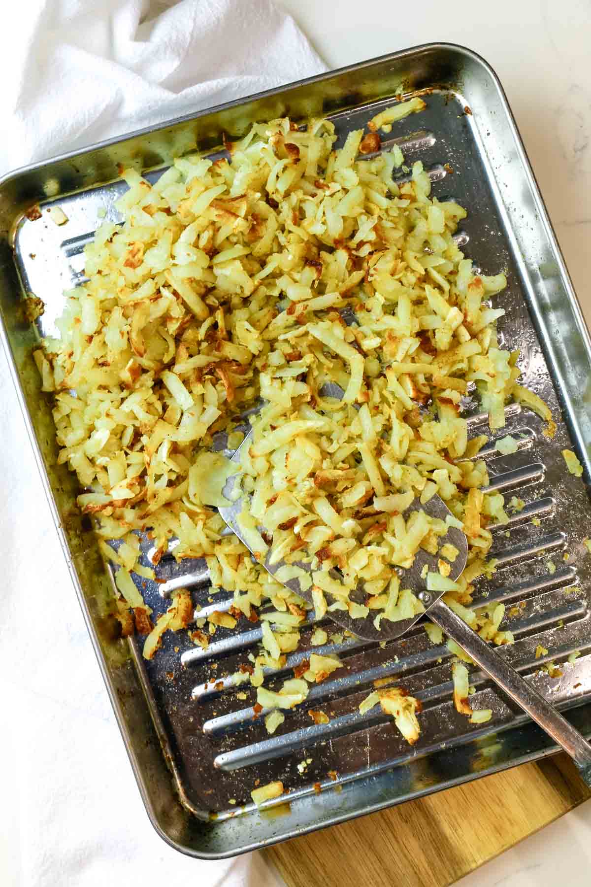 Hash browns on a stainless steel sheet with spatula to make perfectly crispy shredded hash browns in air fyer.