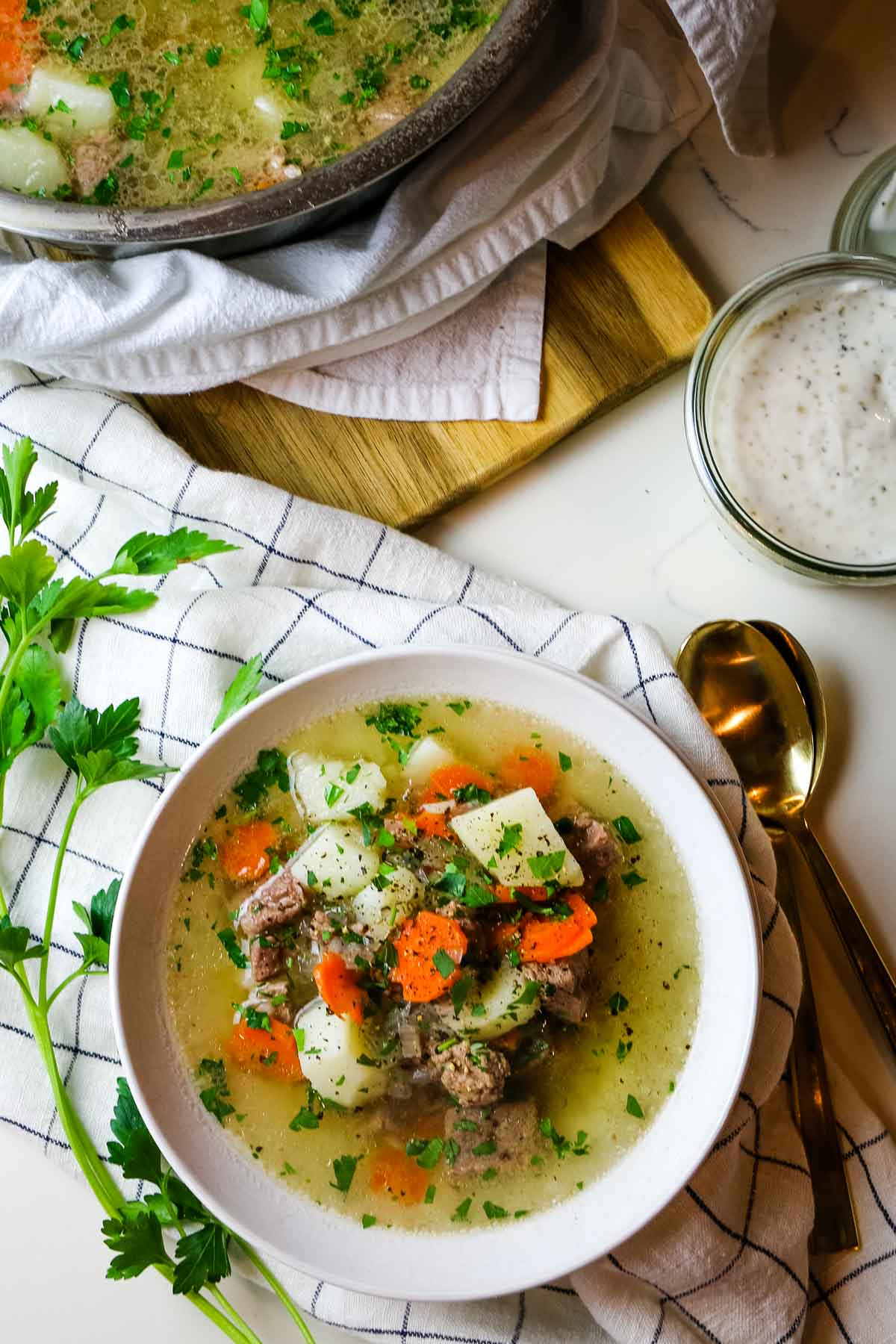 Lamb shurpa soup with carrots and potatoes in white bowl with fresh parsley on the side and a spoon.