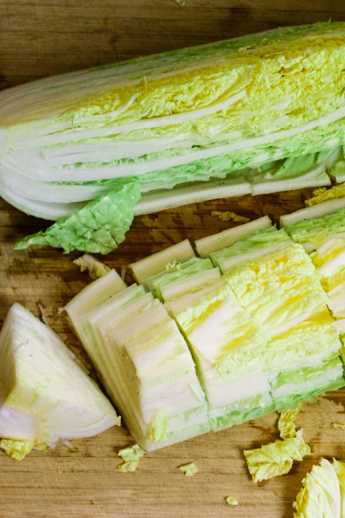 Cutting napa cabbage to prepare kimchi on cutting board.