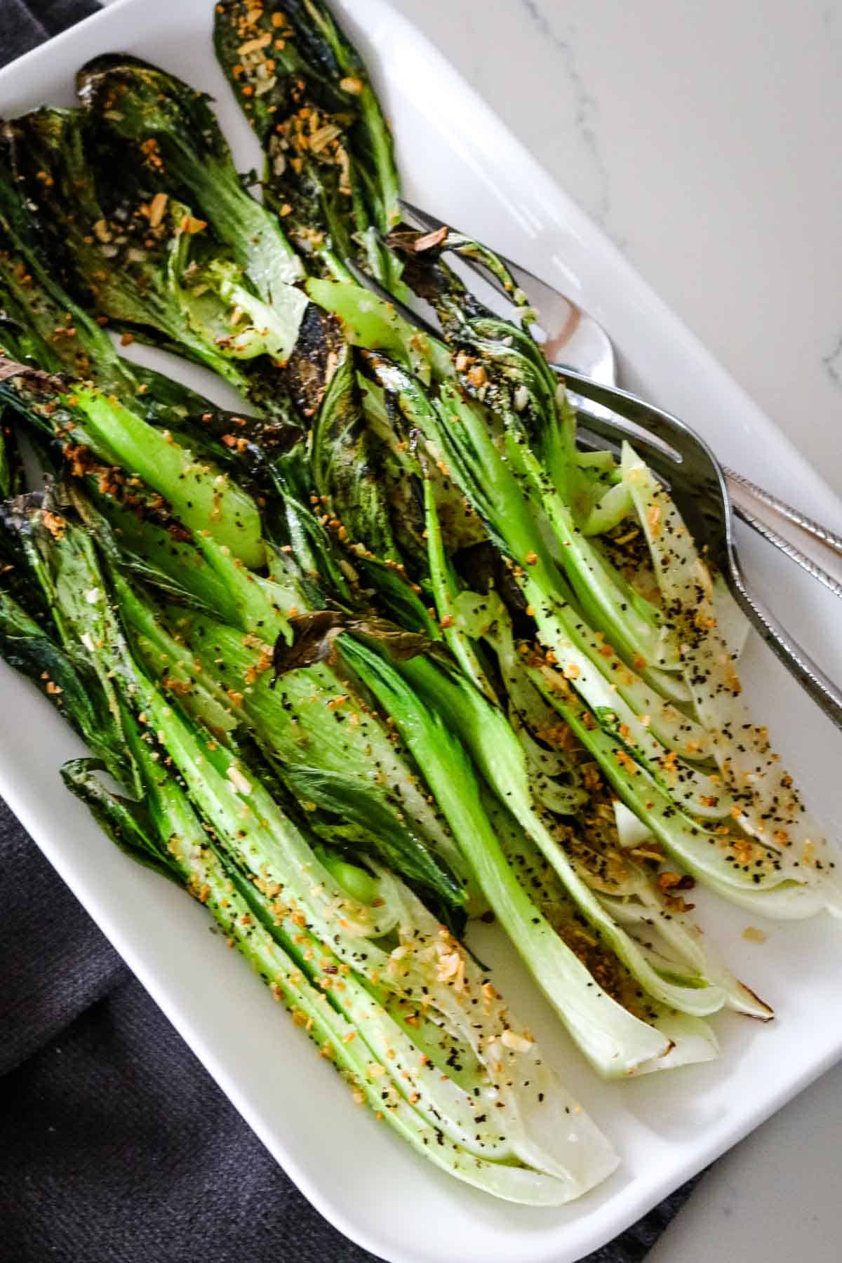 roasted bok choy on white platter with fork.