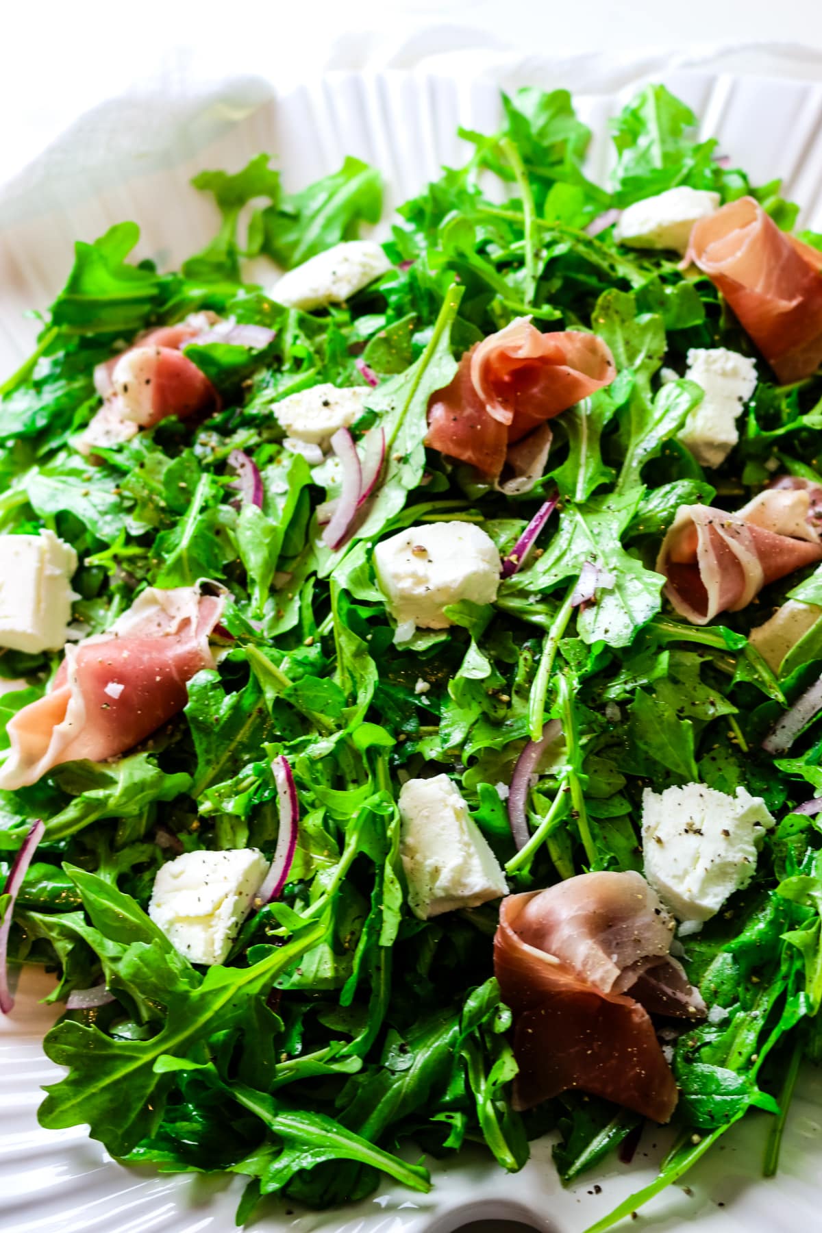 arugula salad with red onions, goat cheese chunks, and wrapped prosciutto on a bed of arugula with cracked black pepper.