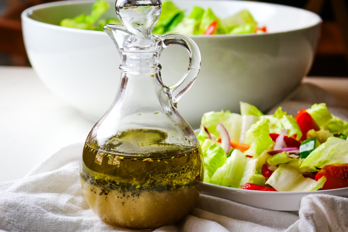 lemon olive oil dressing in a small salad dressing bottle with fresh green salad on the right side.