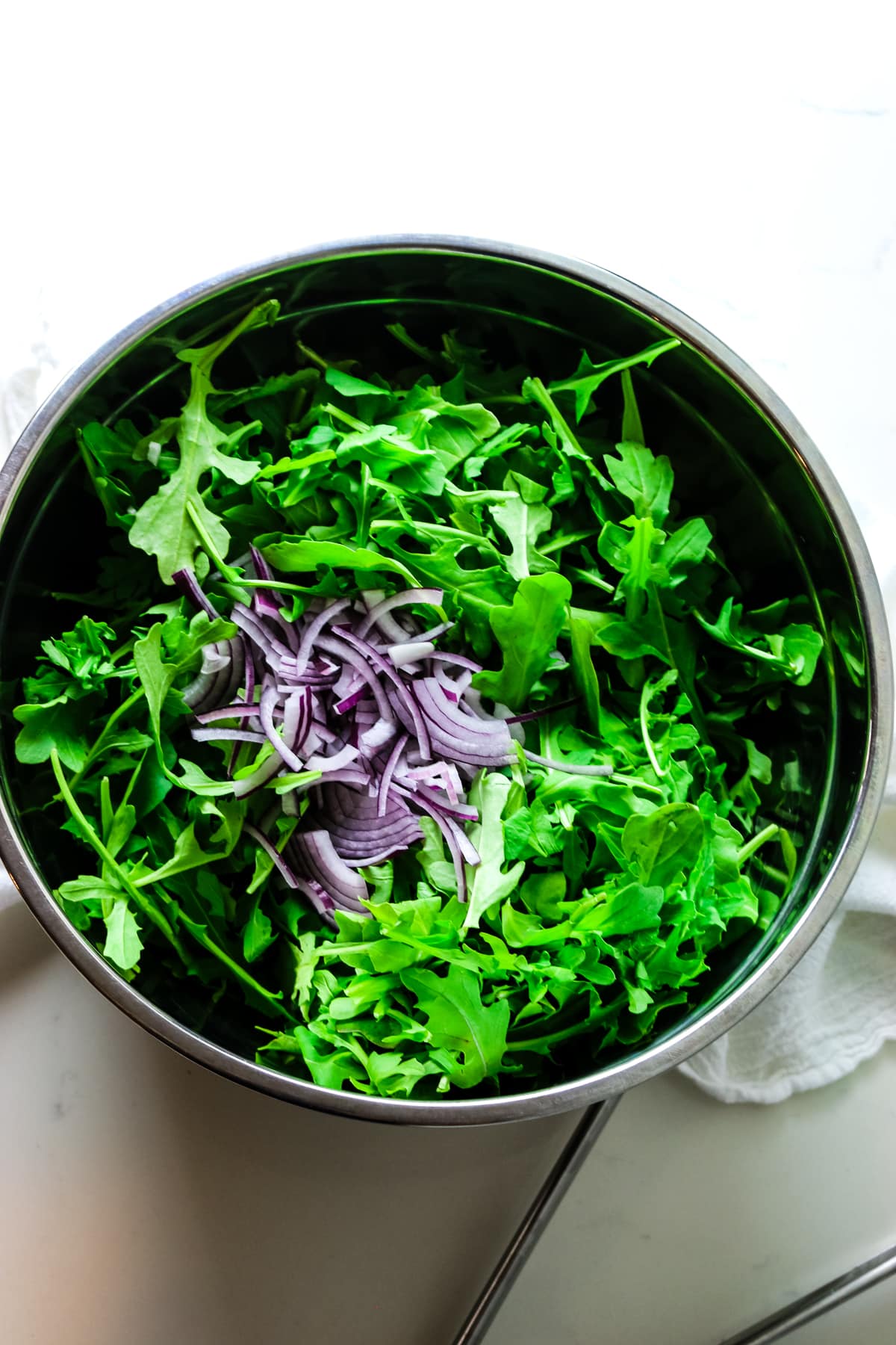 first step in making arugula salad is tossing the arugula or rocket leaves with red onion and salad dressing in large stainless steel bowl.