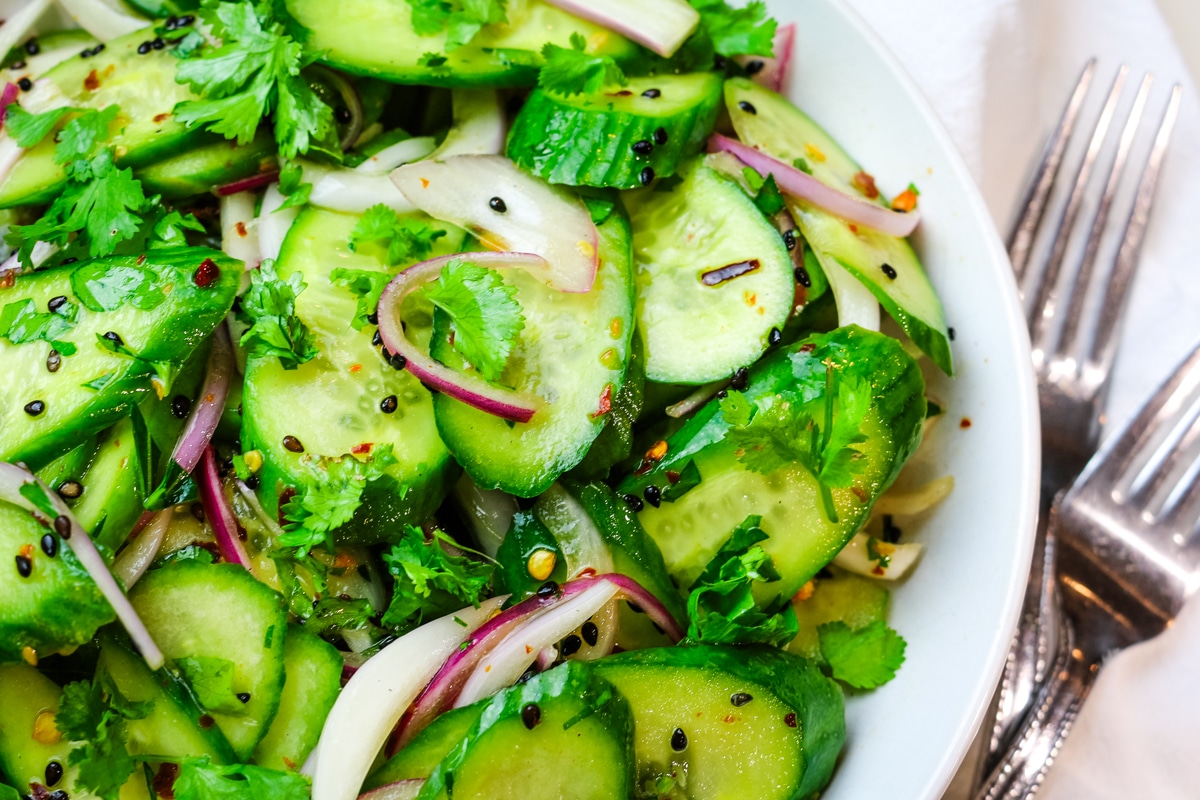 close up of cucumber salad with red pepper flakes and black sesame seeds.