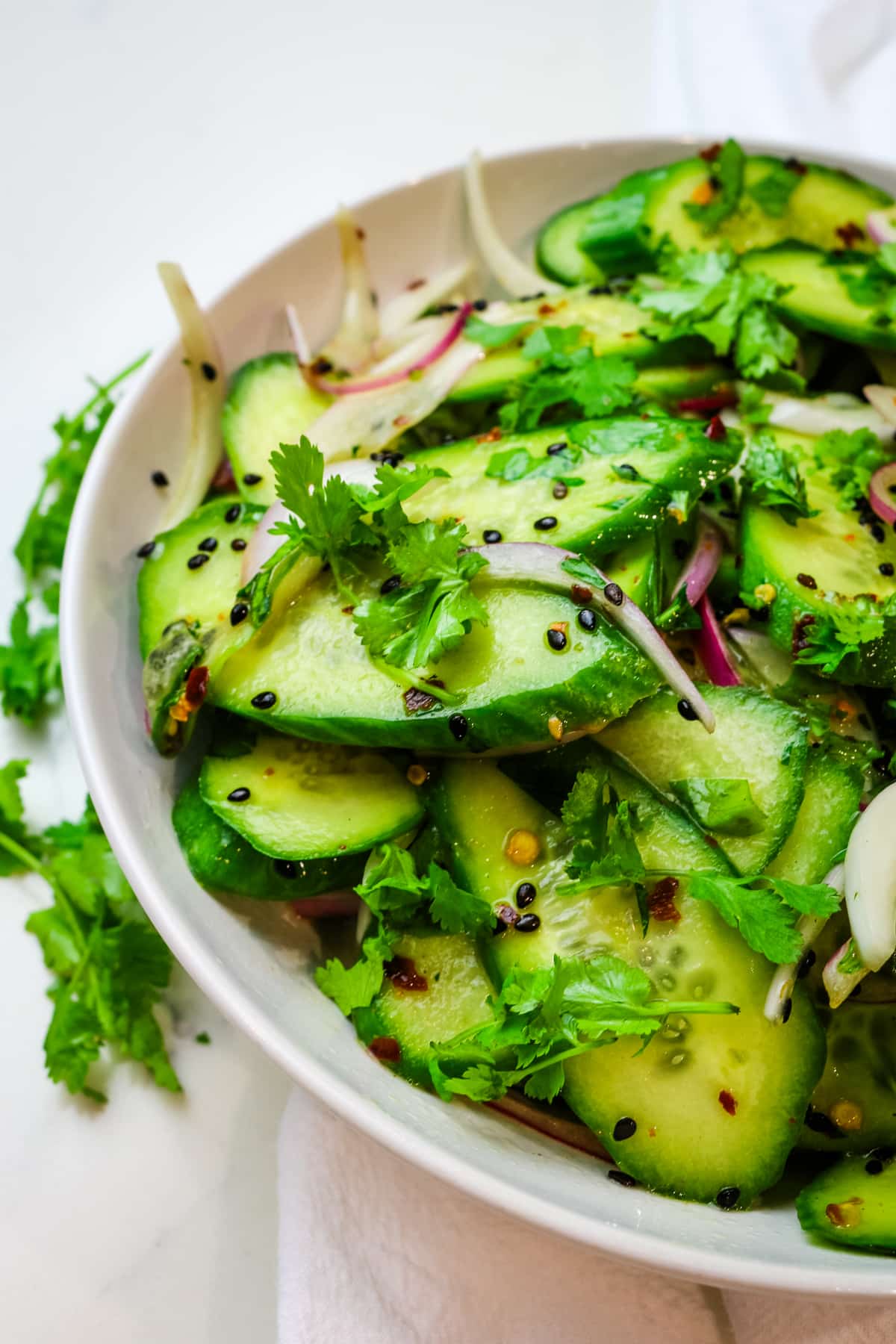Cucumber and fresh cilantro with red onion and black sesame seeds salad in a white bowl.
