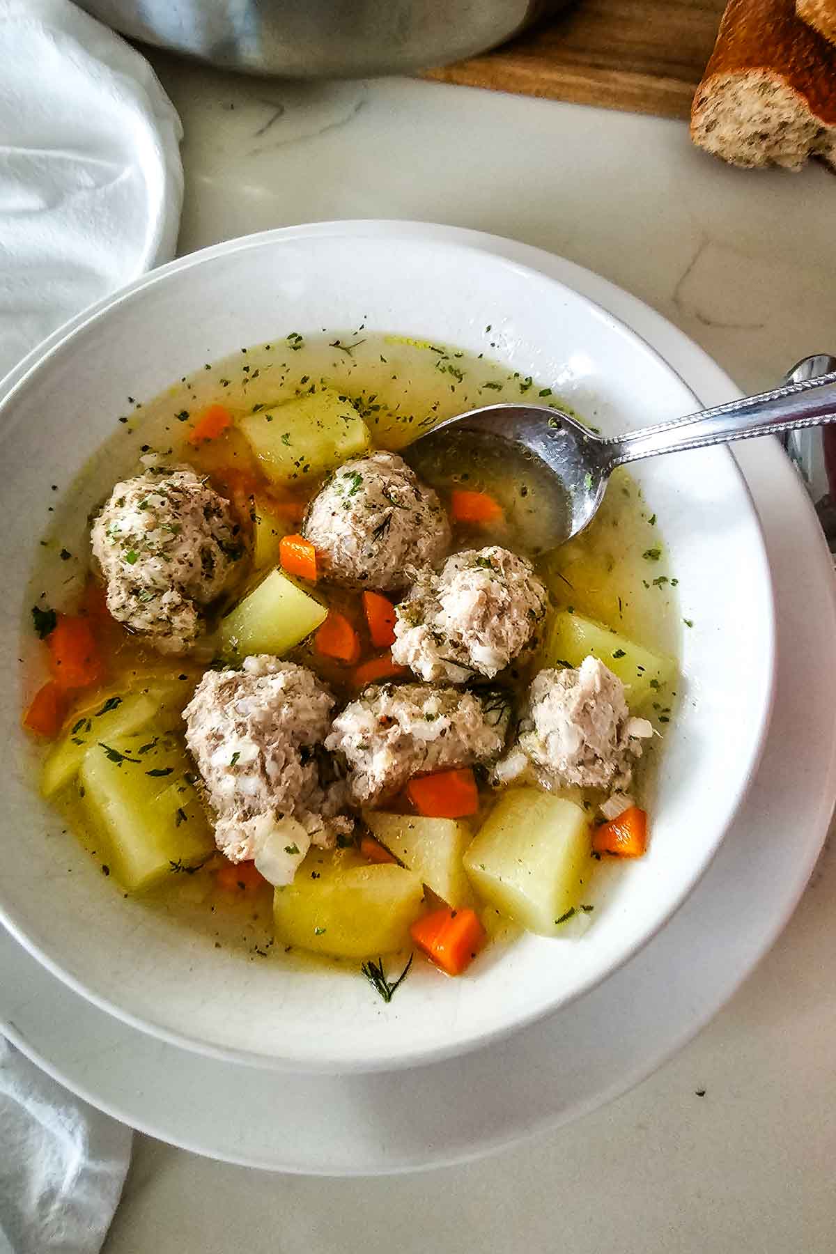 chicken meatball soup with potatoes in white bowl with spoon to the side.