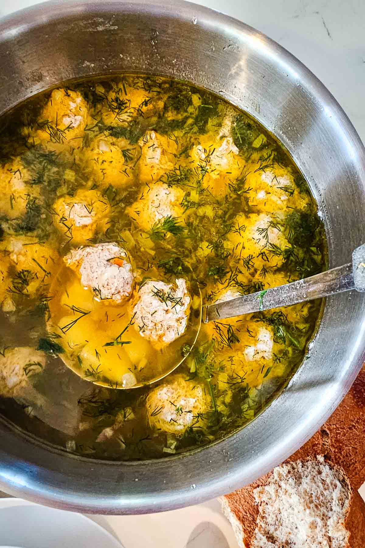 meatball soup in a large pot with a ladle scooping out soup contents.