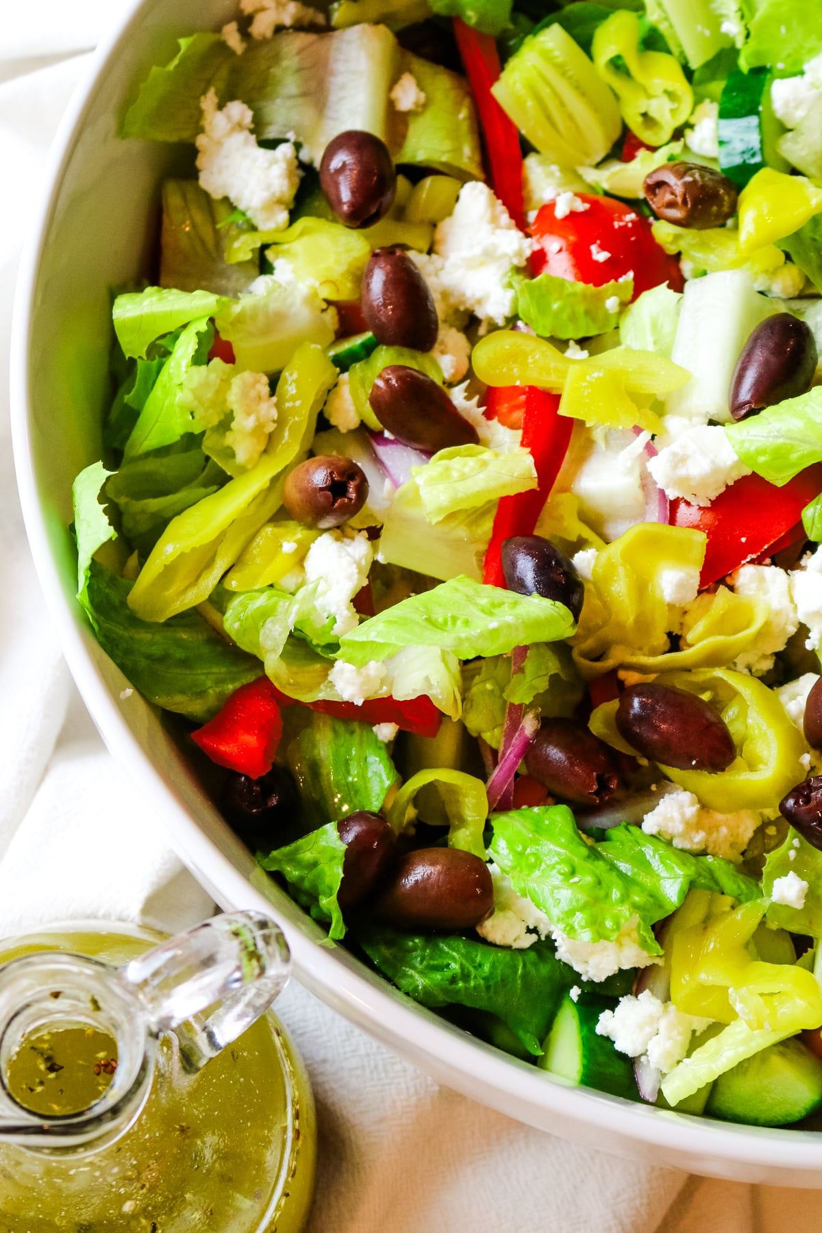 chopped salad in a large white bowl with dressing on the bottom left.