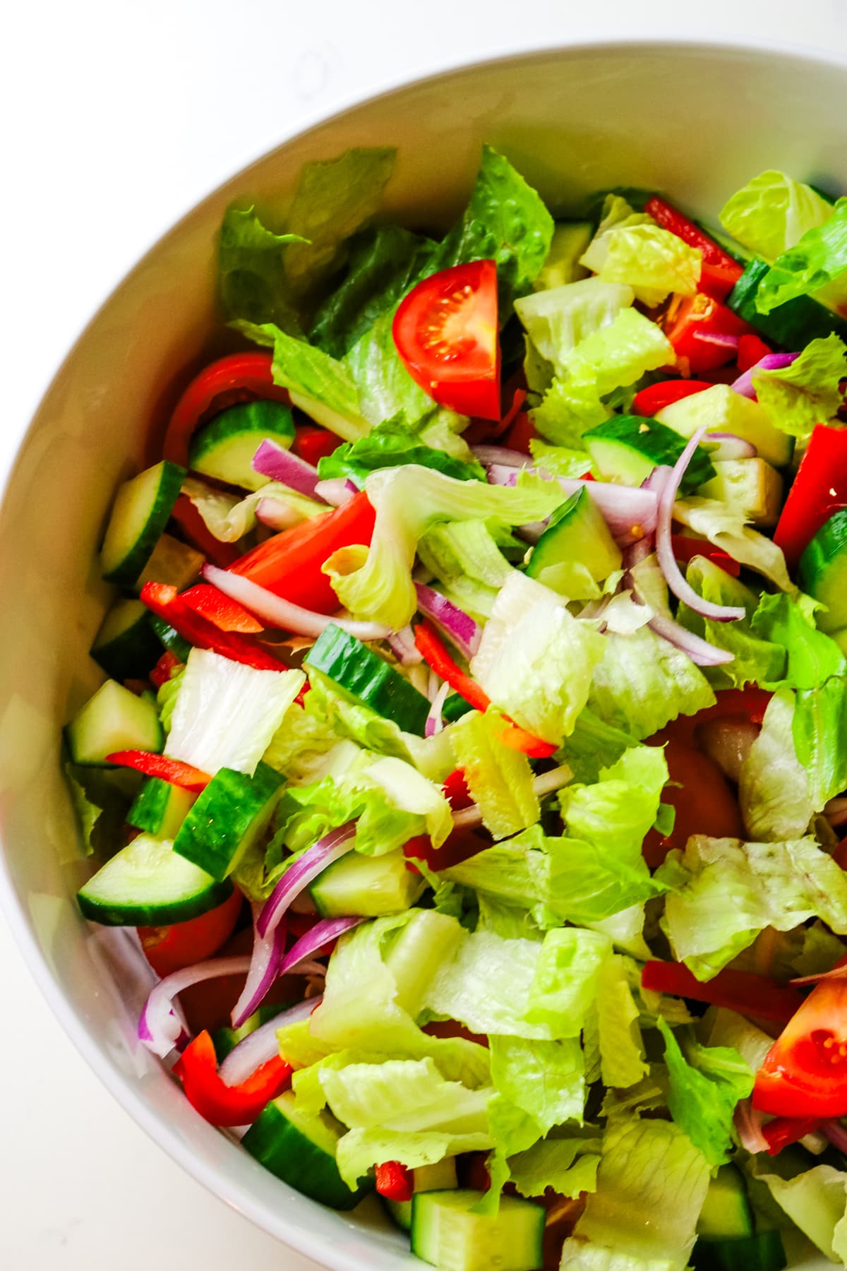 chopped romaine lettuce, red onions, red bell peppers, and tomatoes in a bowl.