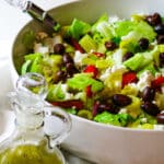 chopped Mediterranean salad in a white bowl with salad dressing on the bottom left corner.