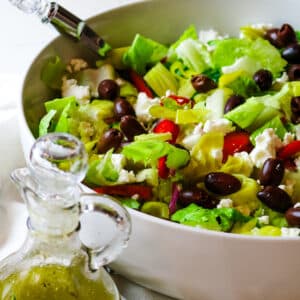 chopped Mediterranean salad in a white bowl with salad dressing on the bottom left corner.