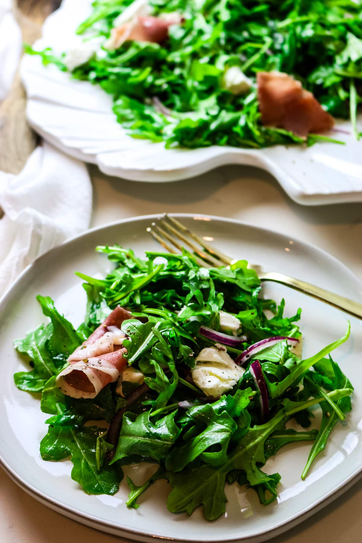a serving of simple arugula salad on a white plate with the serving platter in the background.